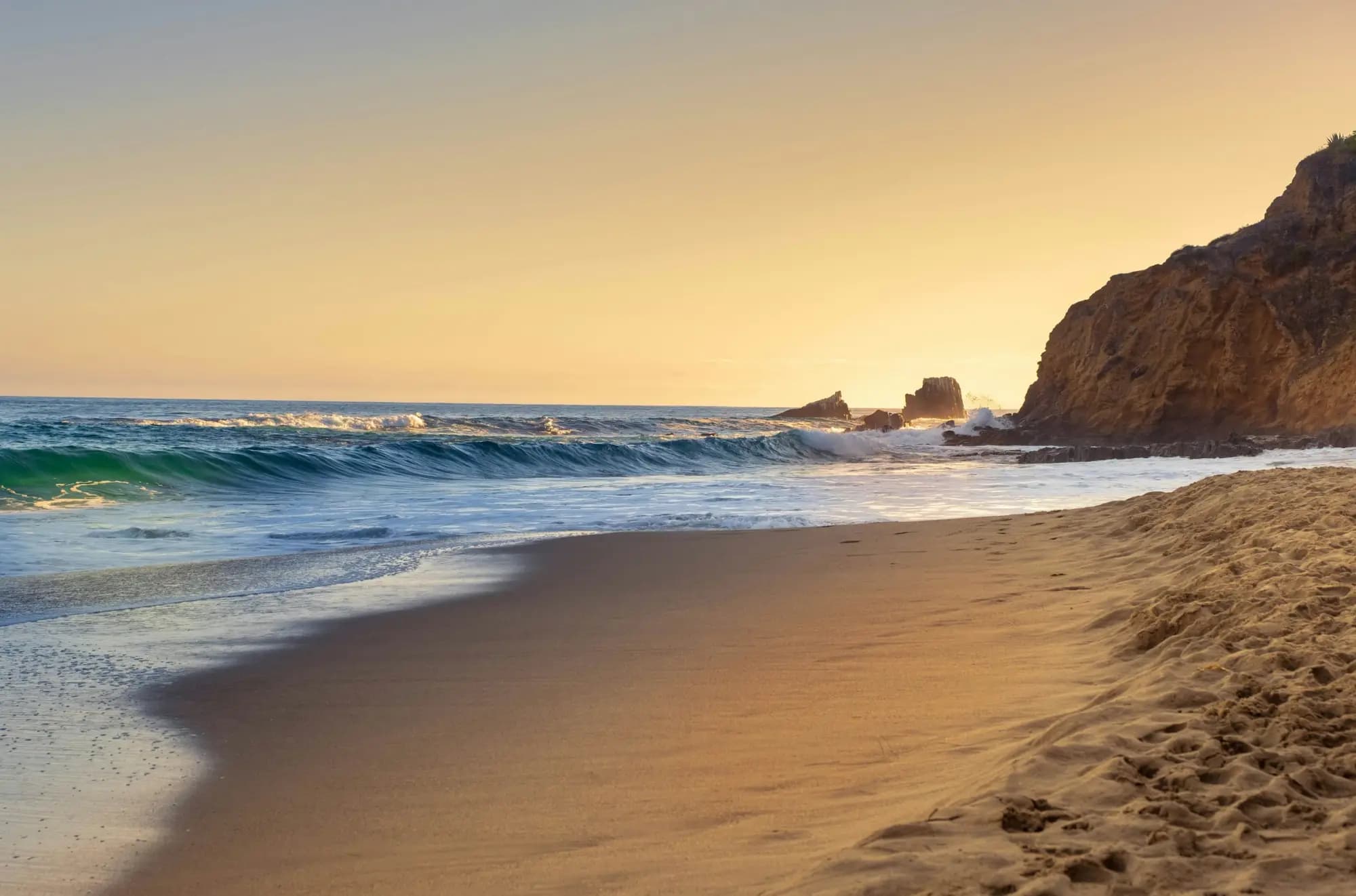 Ondas na areia de Laguna Beach com o penhasco ao fundo na hora dourada